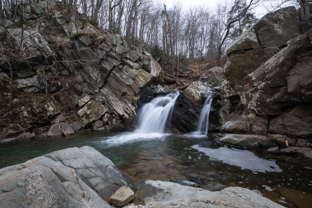 Small waterfall flowing between rocky cliffs into a calm pool in a leafless forest