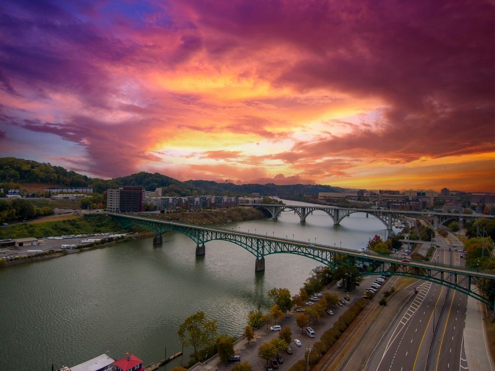 Green bridges span a river at sunset; vibrant orange and purple sky over the city.