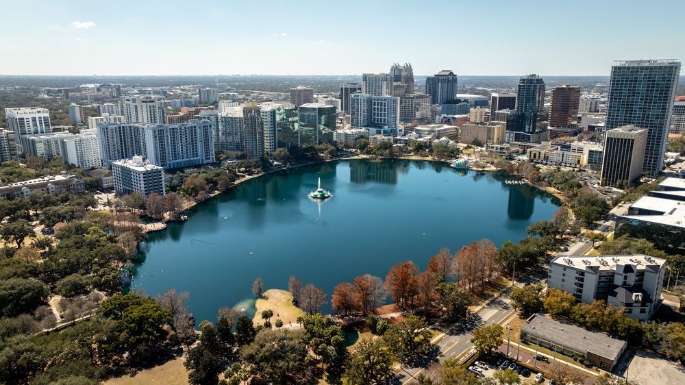 A wide aerial view reveals Lake Eola Park as a green oasis within the heart of downtown Orlando.