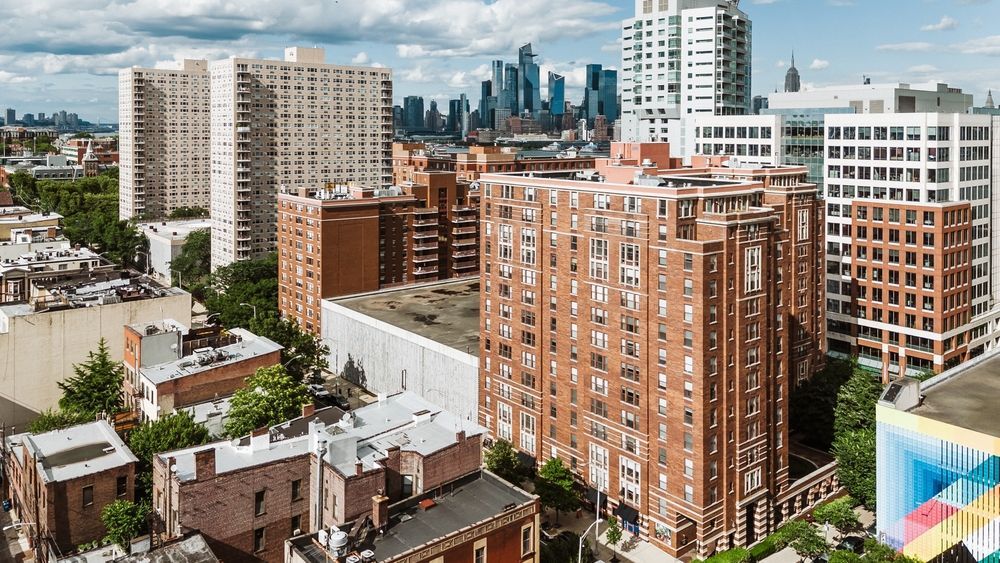 An aerial view of buildings in a city with a distant skyline, featuring red brick and white high-rise structures.