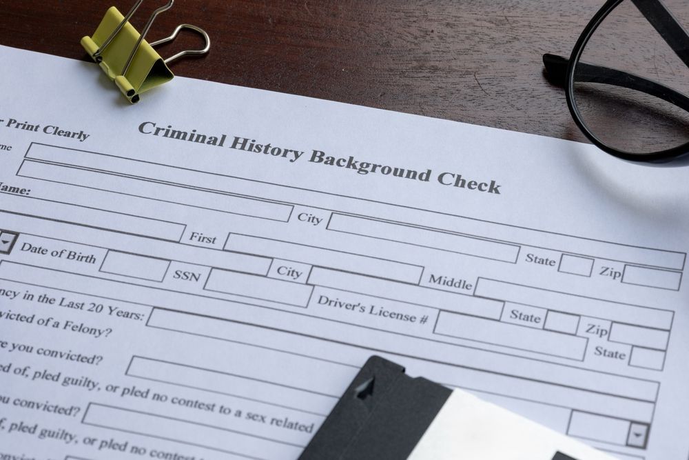Criminal history background check form on a desk with clipboard, glasses, and folded clothing nearby