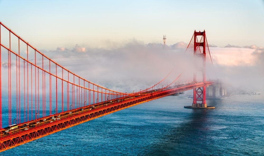 Golden Gate Bridge, San Francisco, partially shrouded in fog; iconic orange bridge spans the blue water.