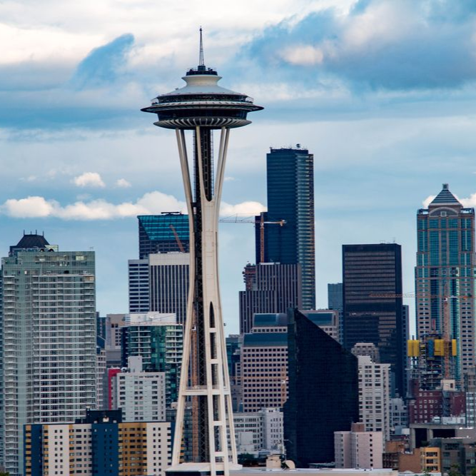 Space Needle with Seattle skyline. Blue sky, white clouds. Tall buildings in background.