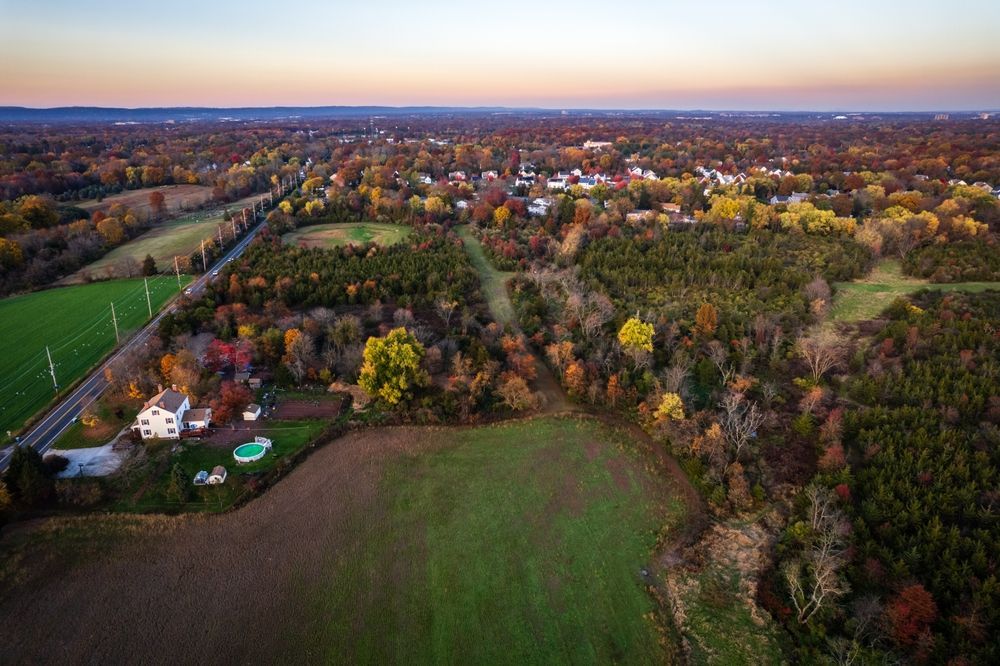 An aerial view of a rural landscape at sunset with a farmhouse, a large open field, and a small town in the distance. Aerial Drone Of Somerset Sunset