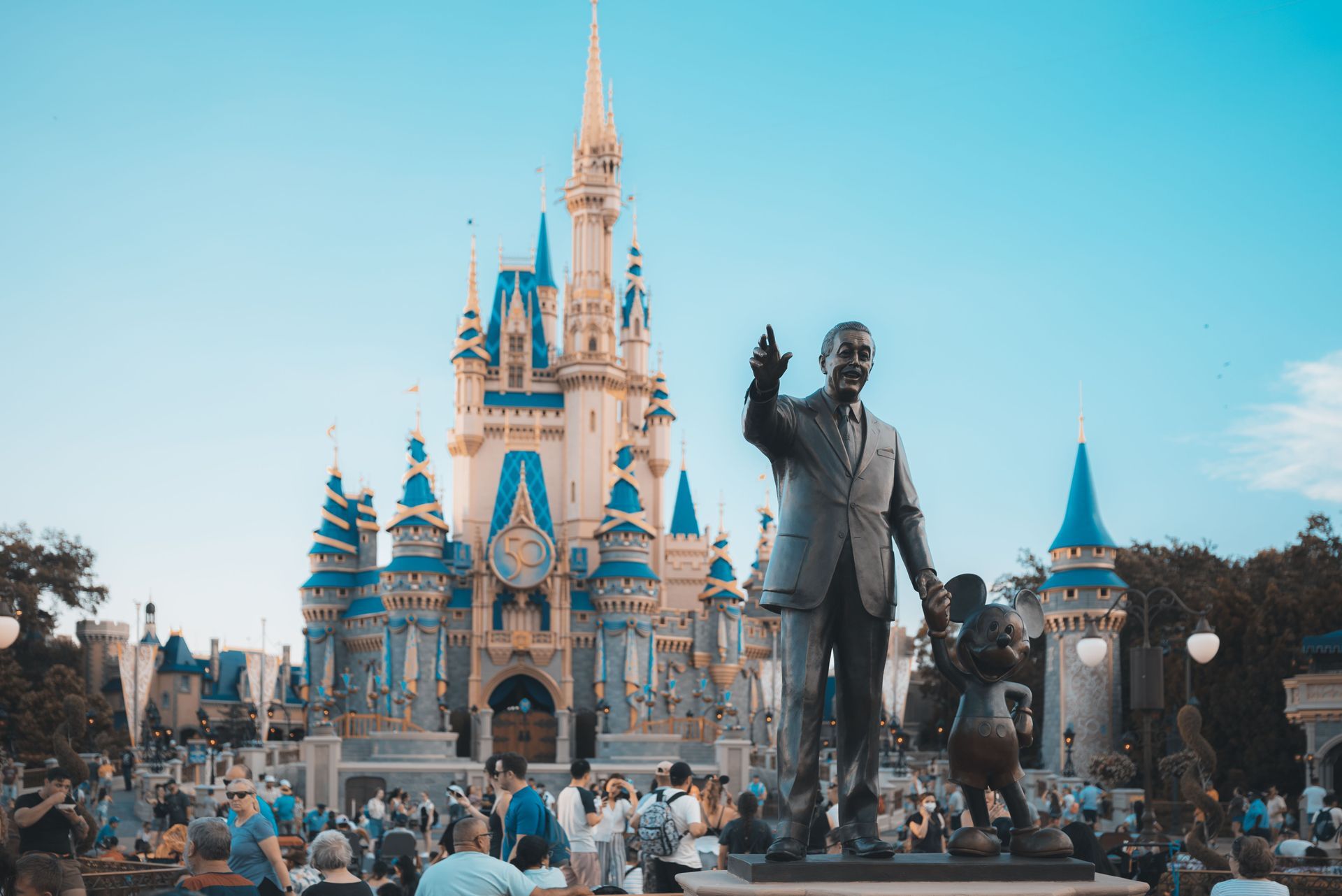 Cinderella Castle with a statue of Walt Disney in front, surrounded by park visitors under a clear blue sky