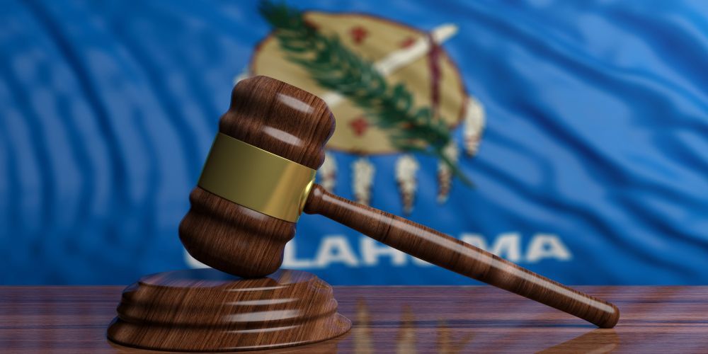 A wooden judge 's gavel is sitting on a wooden table in front of an oklahoma flag.