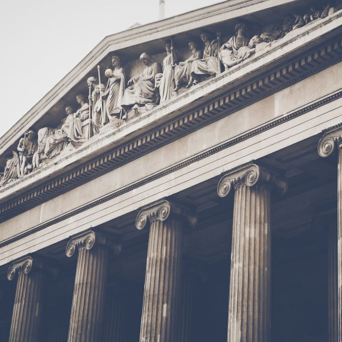 Classical building exterior with fluted columns, a triangular pediment, and sculptures.