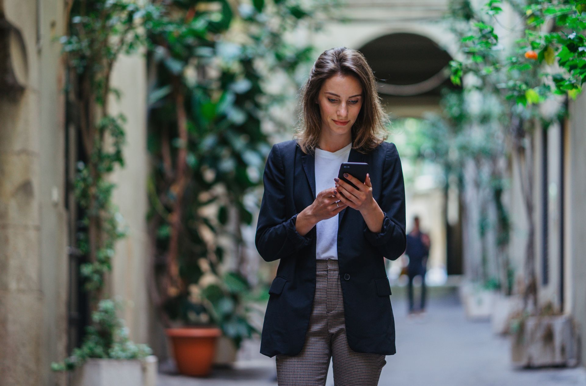 a female court runner, CRA reviews background screening trends on her smart phone walking through a picturesque alley