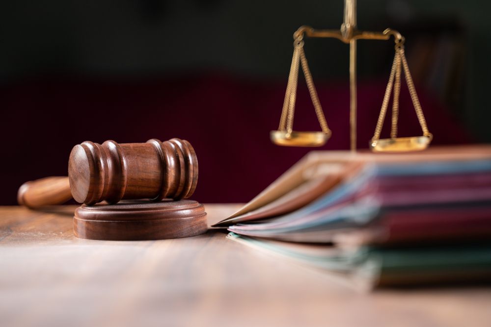 Wooden gavel and scales of justice on a table with documents, representing legal proceedings.