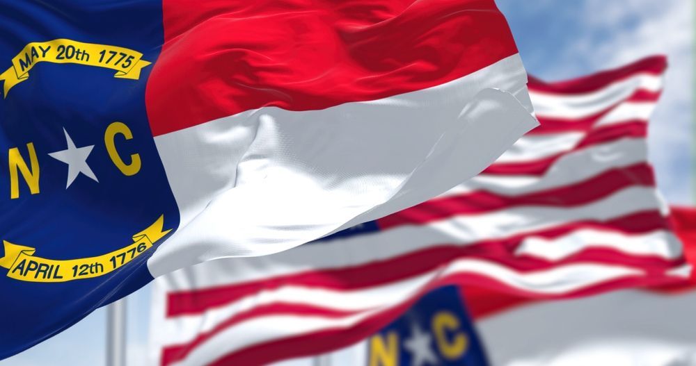 North Carolina flags waving against a blue sky, with a U.S. flag in the background