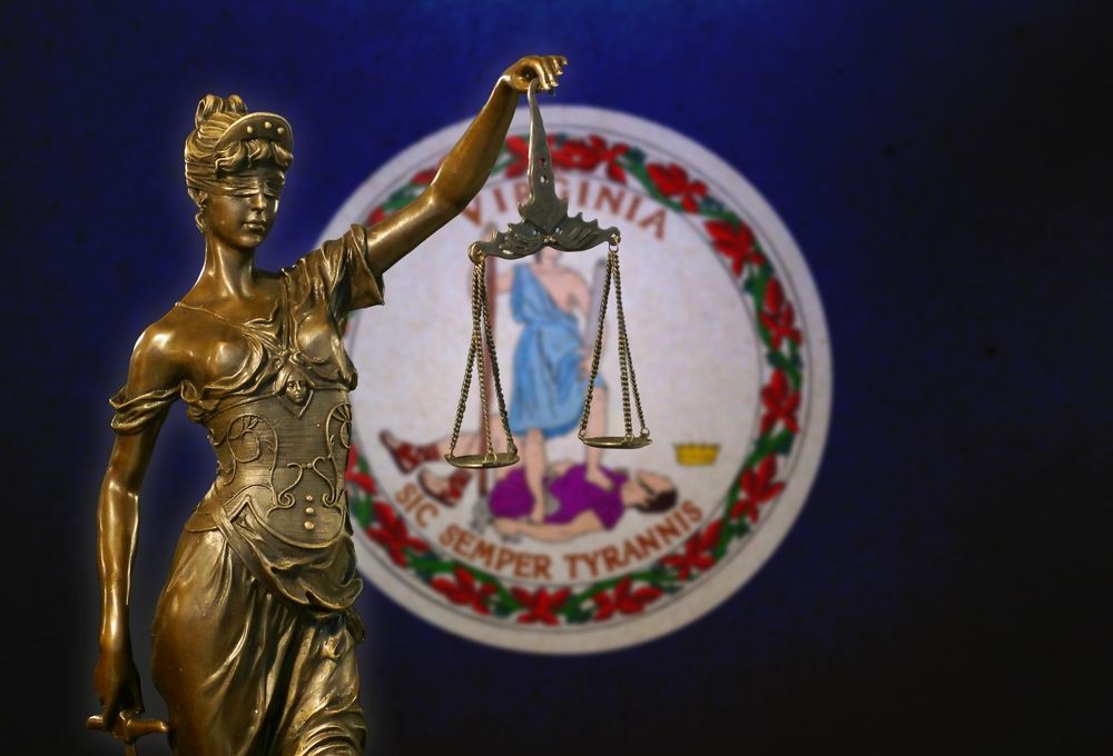 Statue of Lady Justice holding scales in front of the Virginia state flag.