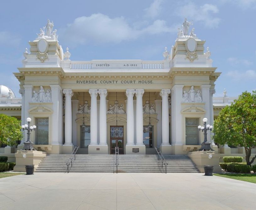 Riverside County Courthouse exterior with white columns, light-colored walls, and steps leading to the entrance, under a blue sky.