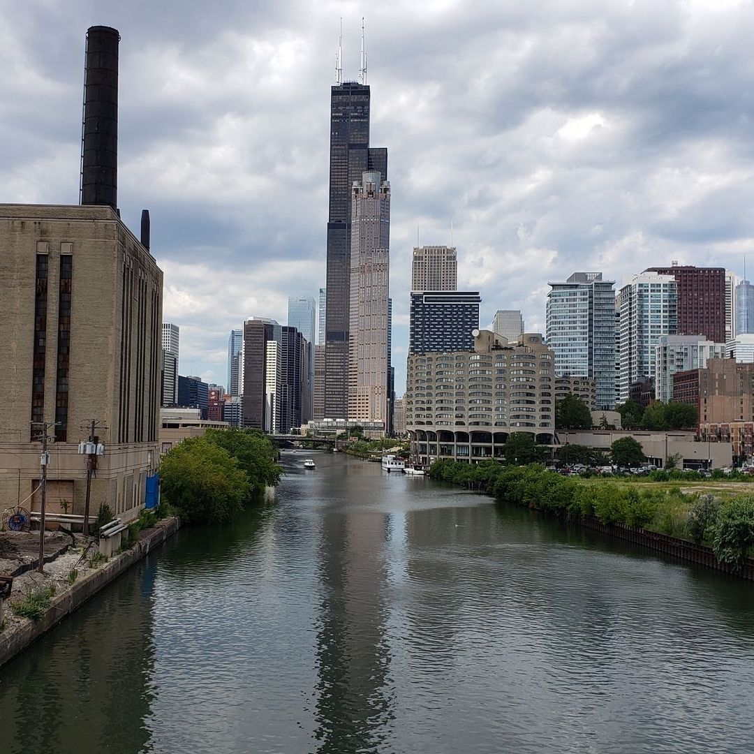 Chicago River with skyscrapers, including the Willis Tower, and a cloudy sky overhead.