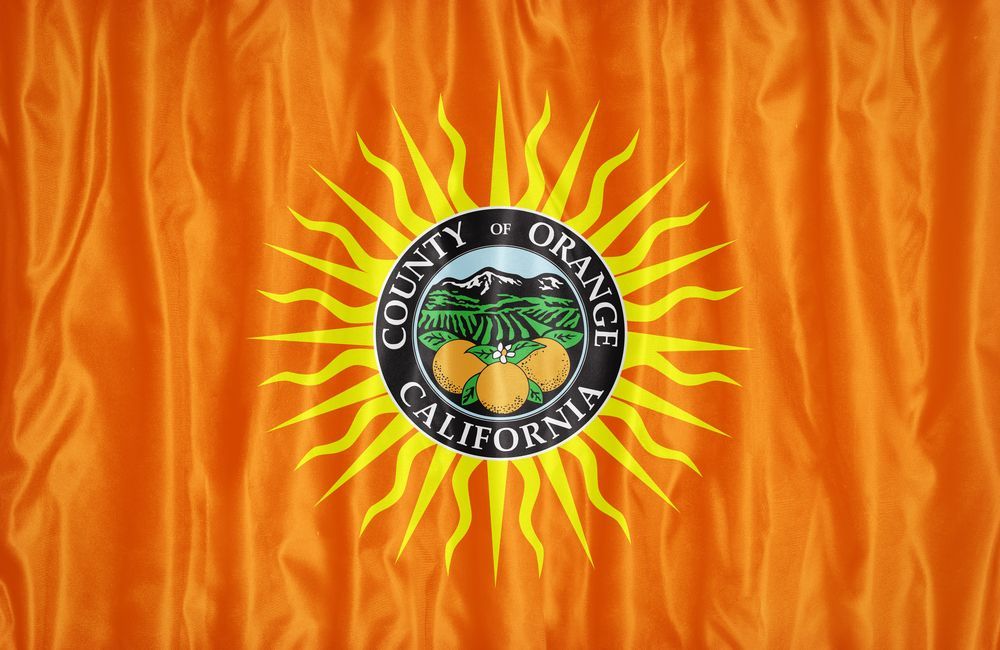 Orange County, California flag. A sunburst design with a central seal depicting oranges, fields, and mountains on an orange background.