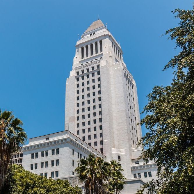 Los Angeles City Hall, a tall, white art deco building under a clear blue sky, framed by palm trees.