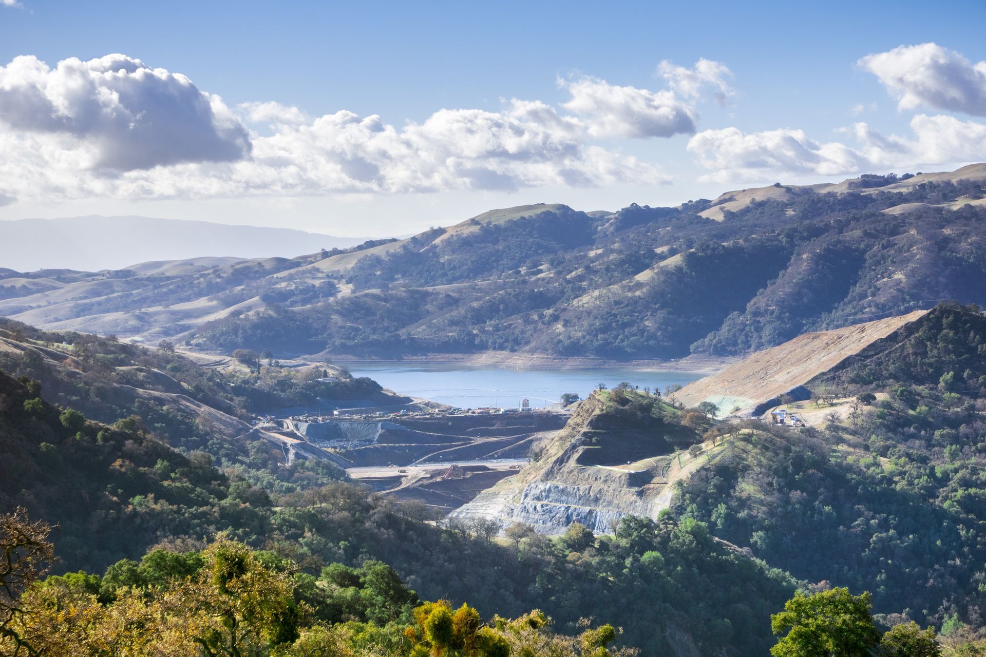 Hilly landscape with a lake nestled between the mountains under a partly cloudy sky.