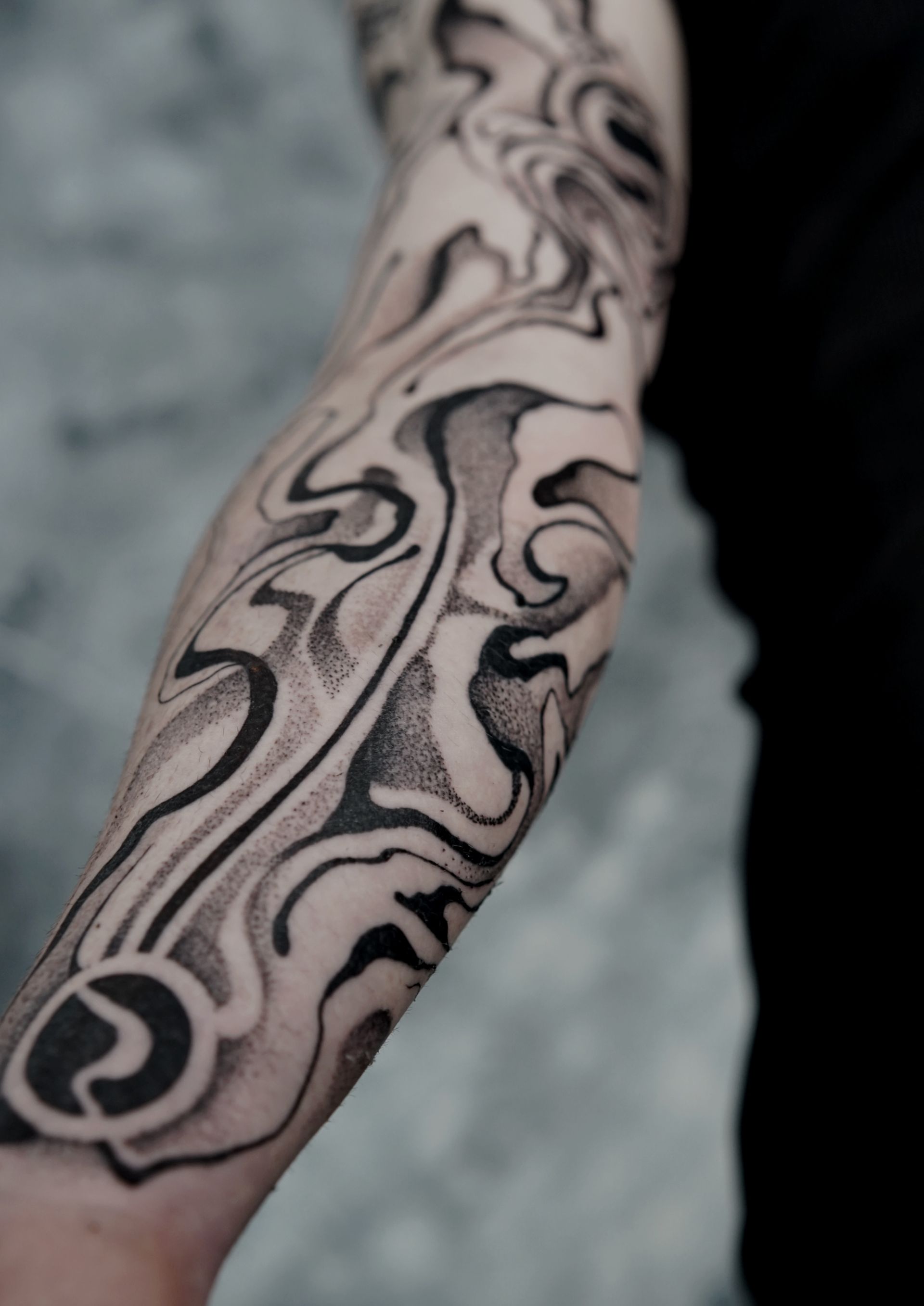 Arm covered in abstract black and gray swirling tattoo.