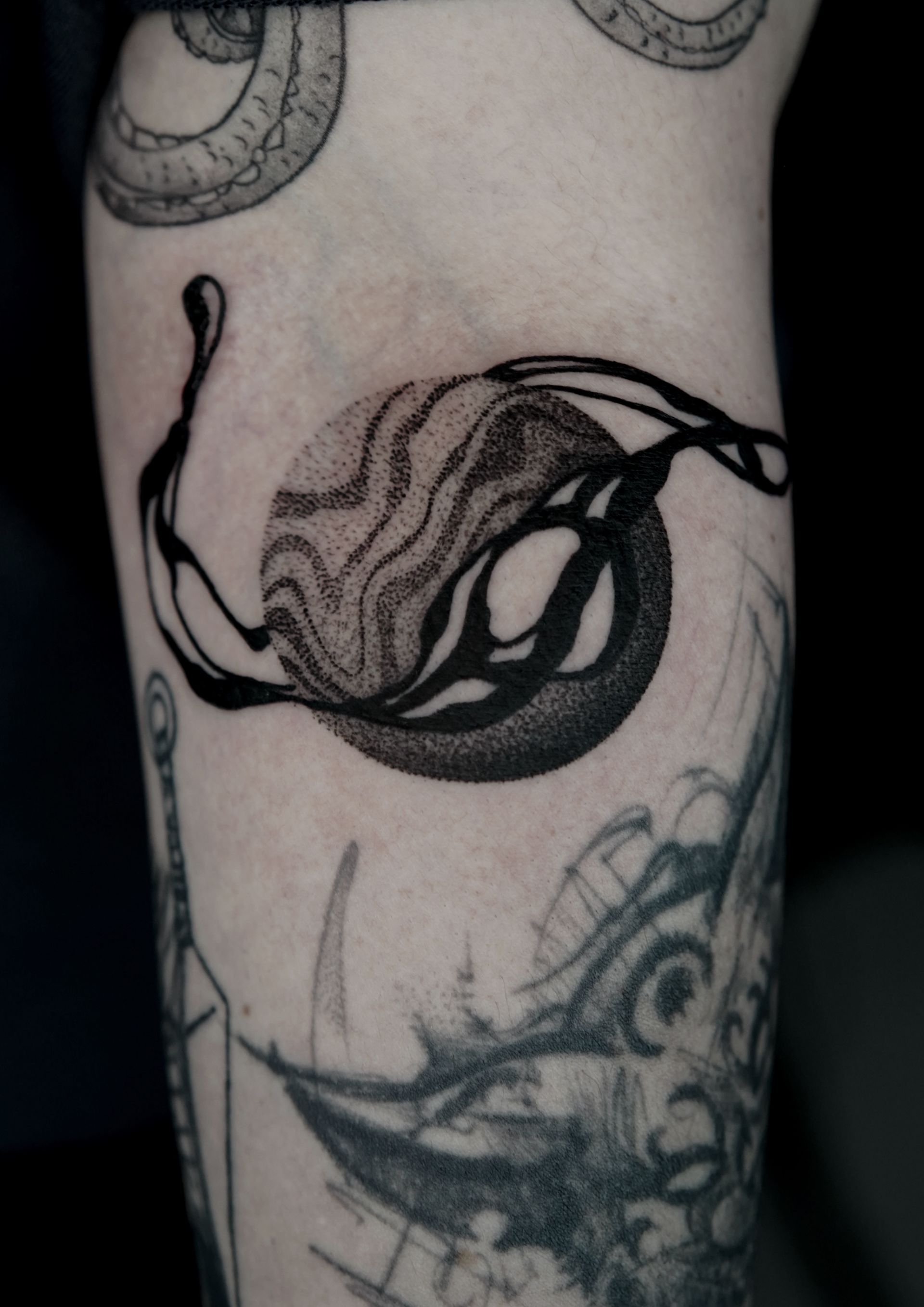 Black tattoo on skin, circular design with flowing lines and stippling effect.