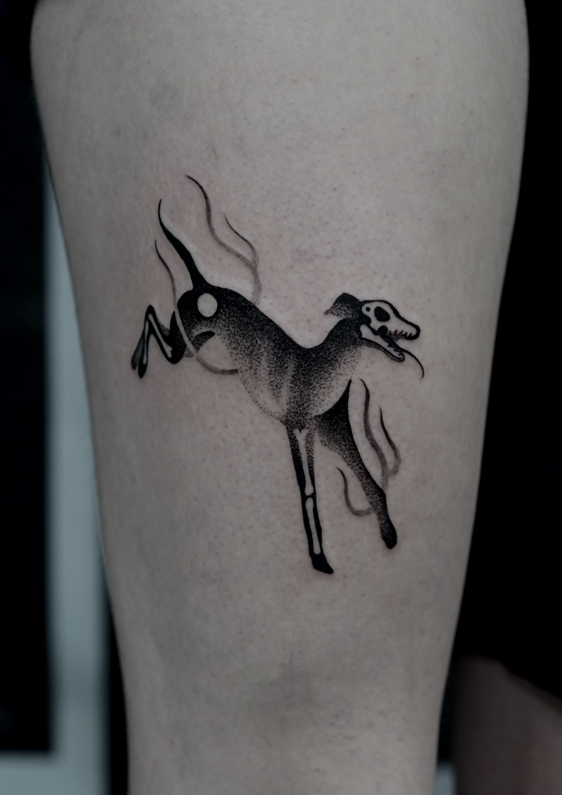 Black tattoo of a stylized leaping dog on a leg, detailed with dot-work.