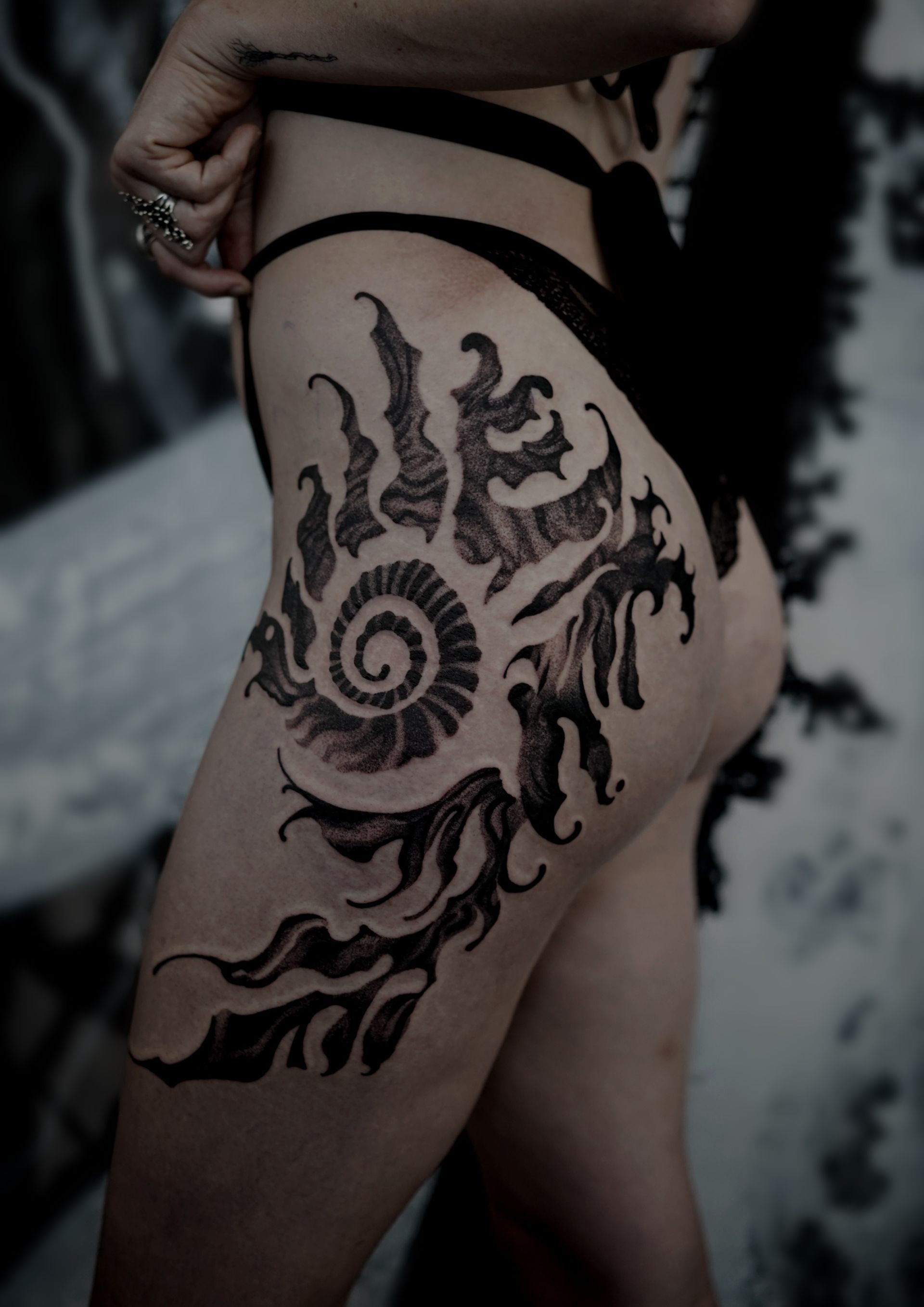 Black tattoo on a person's upper thigh. The design includes a spiral, swirls, and abstract shapes.