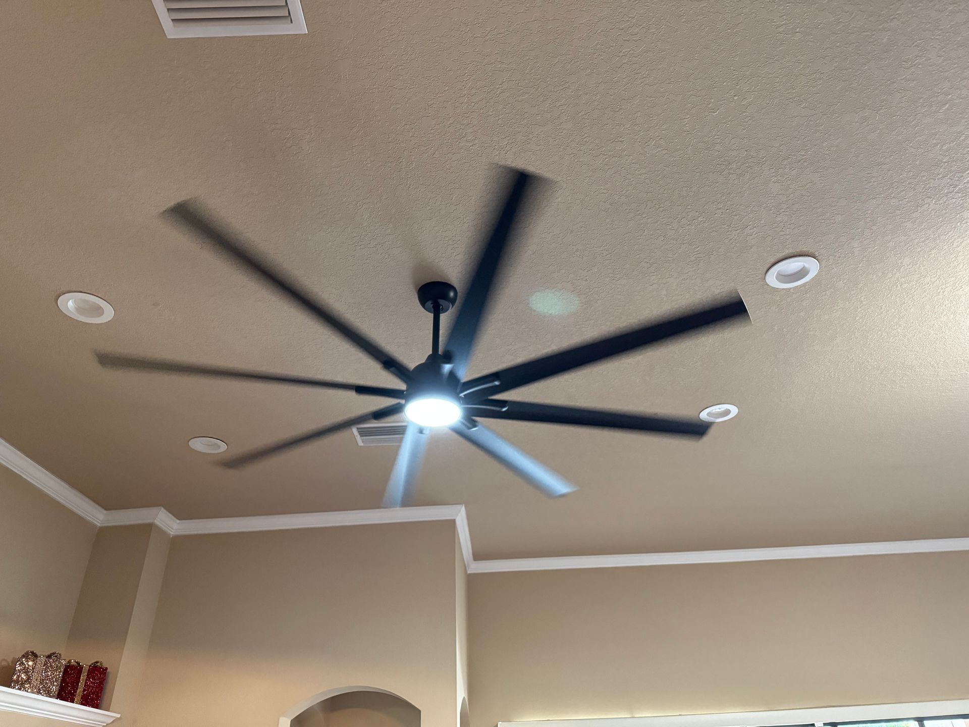 Ceiling fan with dark blades and bright light on a beige room ceiling