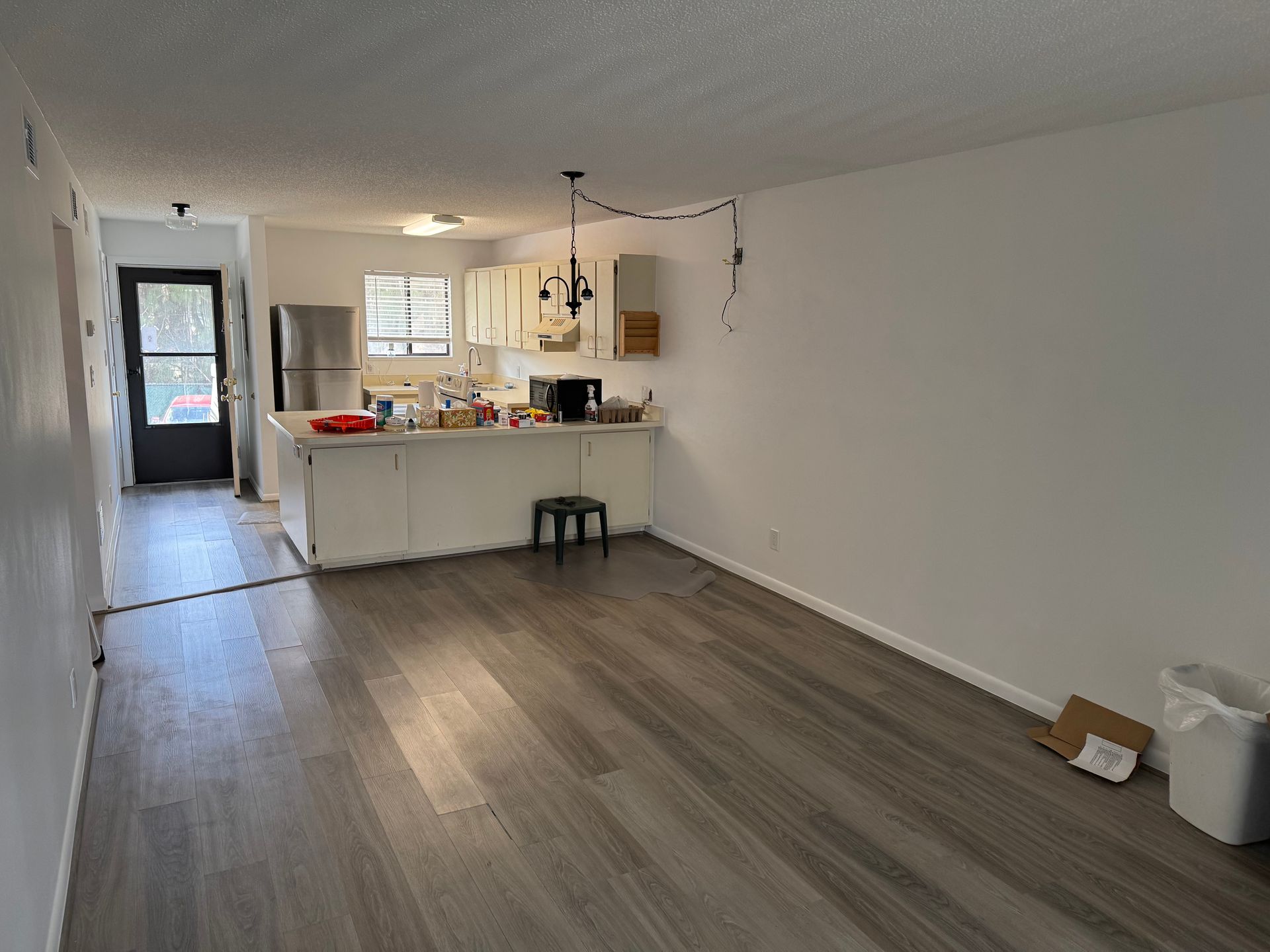 Empty open-plan kitchen and living room with wood floors, white walls, and a black front door.