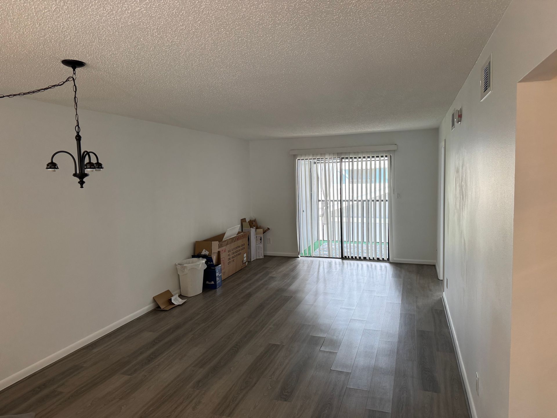 Empty unfurnished living room with wood floors, white walls, and sliding glass doors at the far end