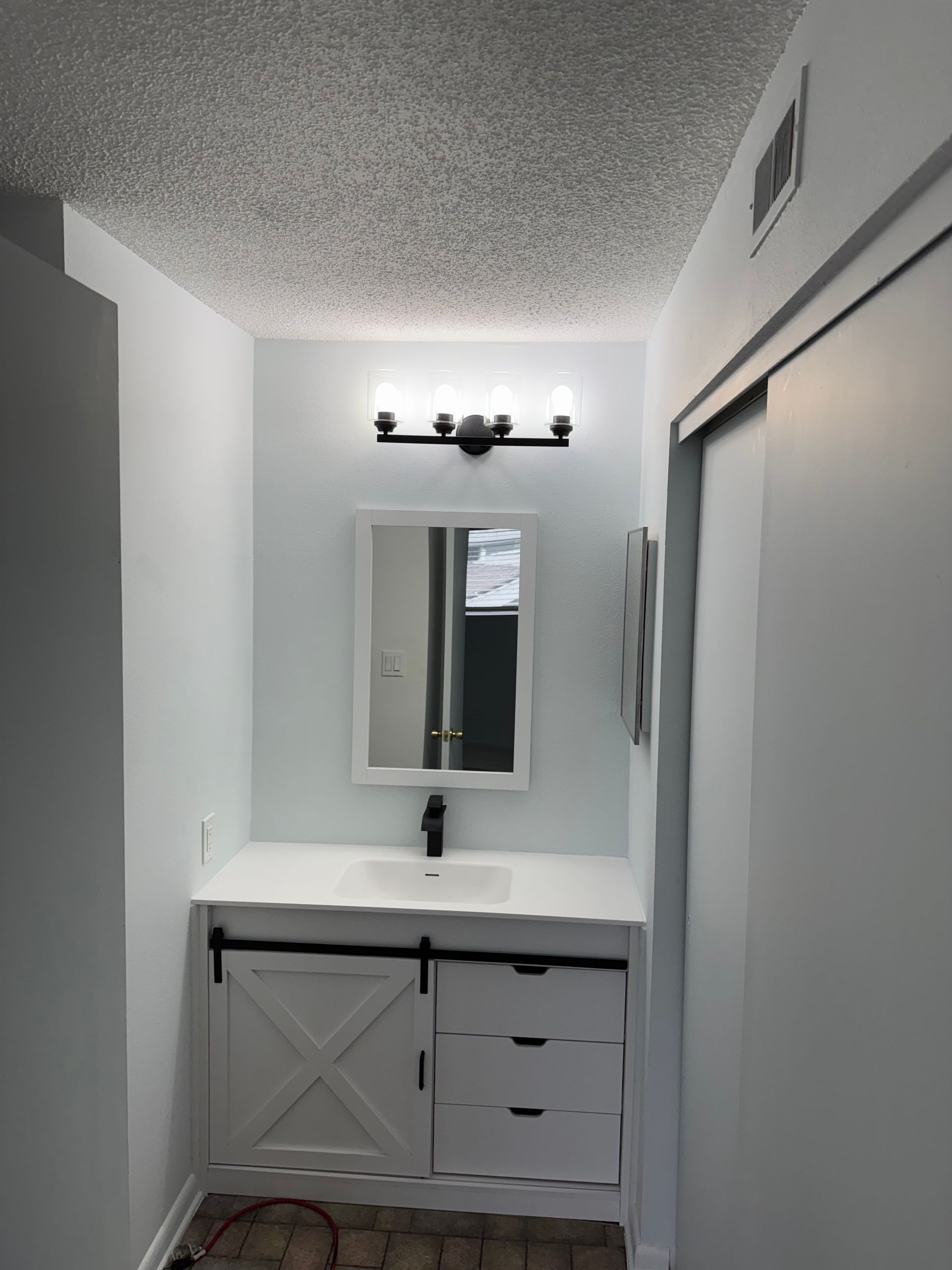 Narrow white bathroom with vanity, mirror, and overhead light above a sink.