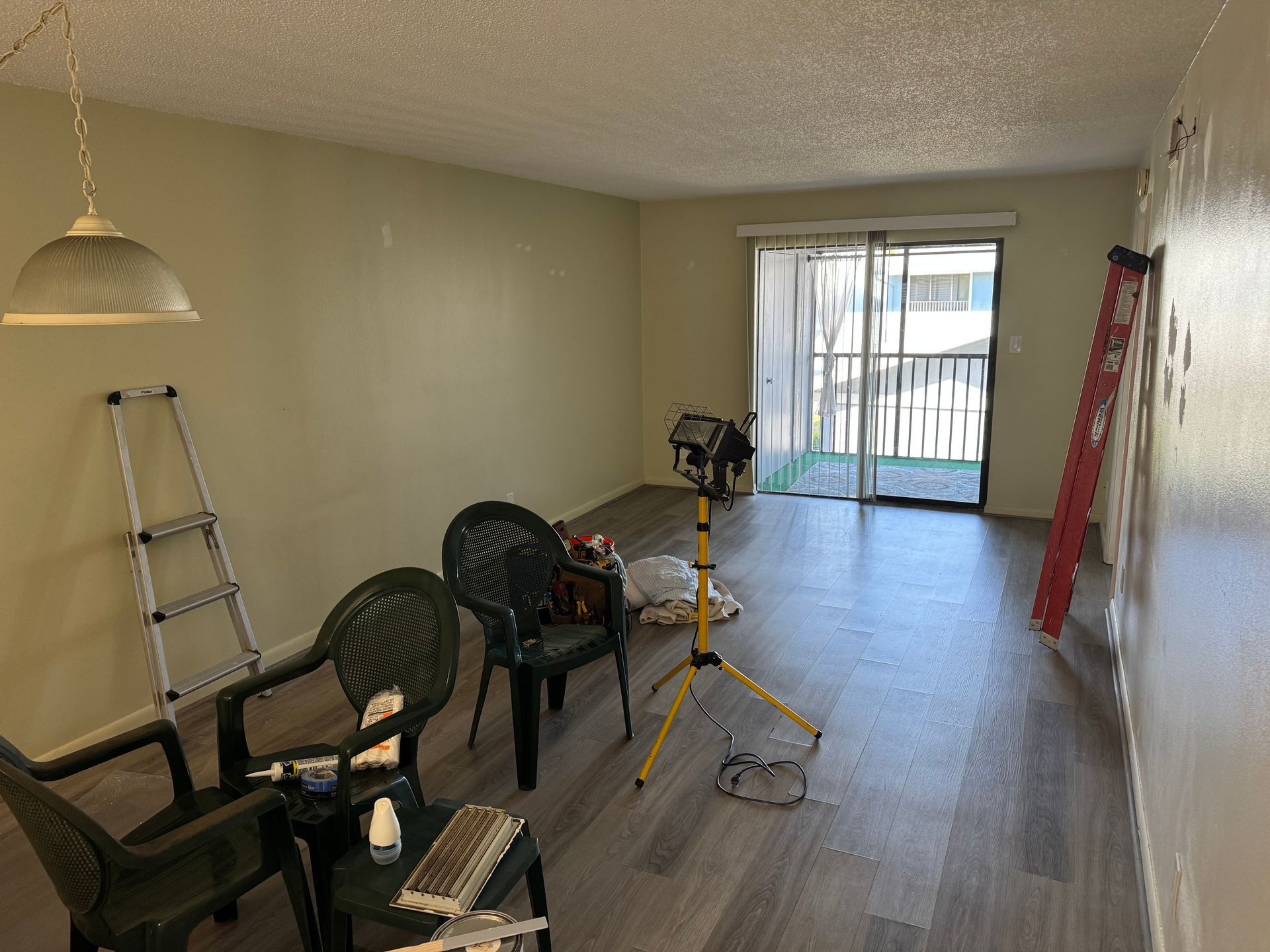 Empty room with ladder, chairs, tools, and sliding glass door to balcony