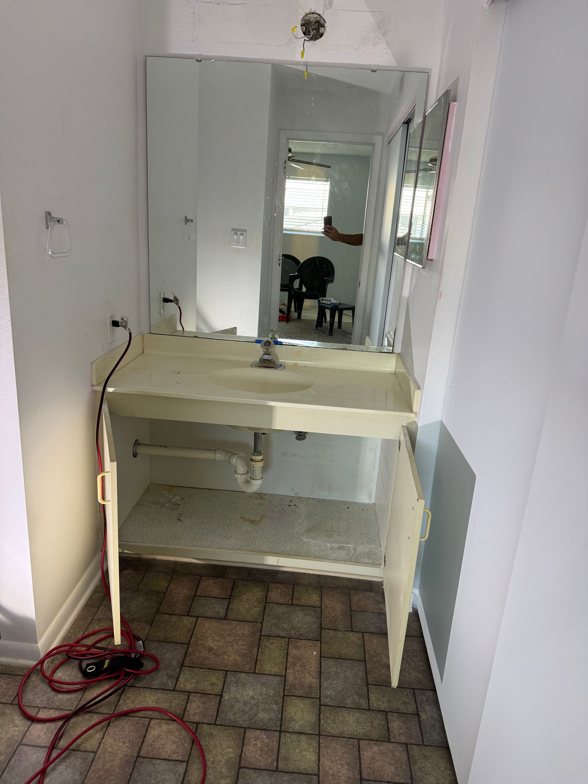 Old vanity with mirror in a narrow hallway; a coiled red cord lies on the brick floor.