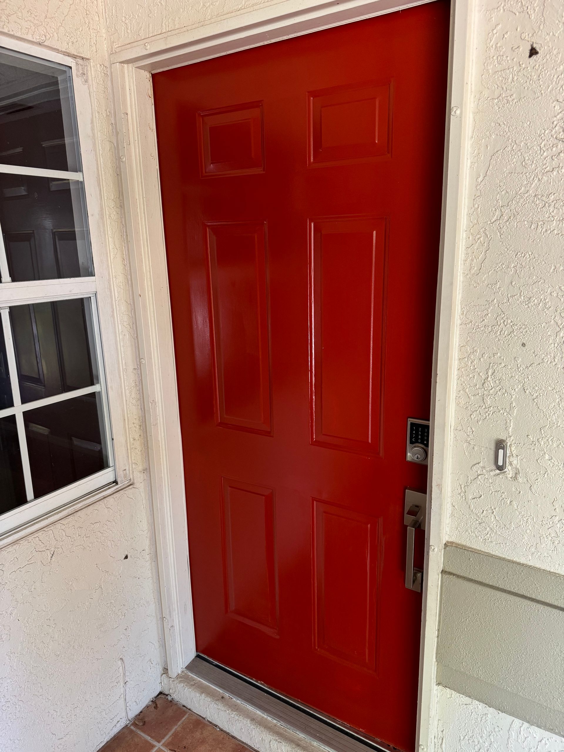 Red front door beside a window on a stucco porch.