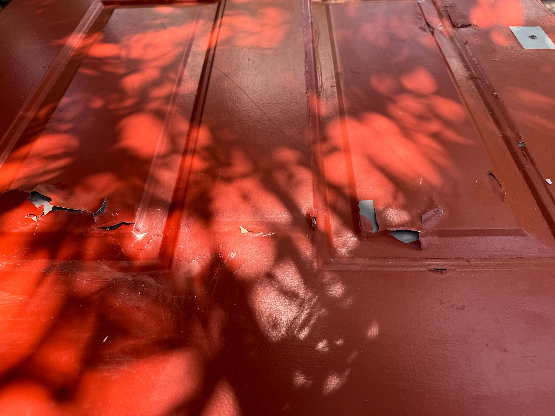 Red wooden deck with leaf shadows and scattered screws near a door threshold