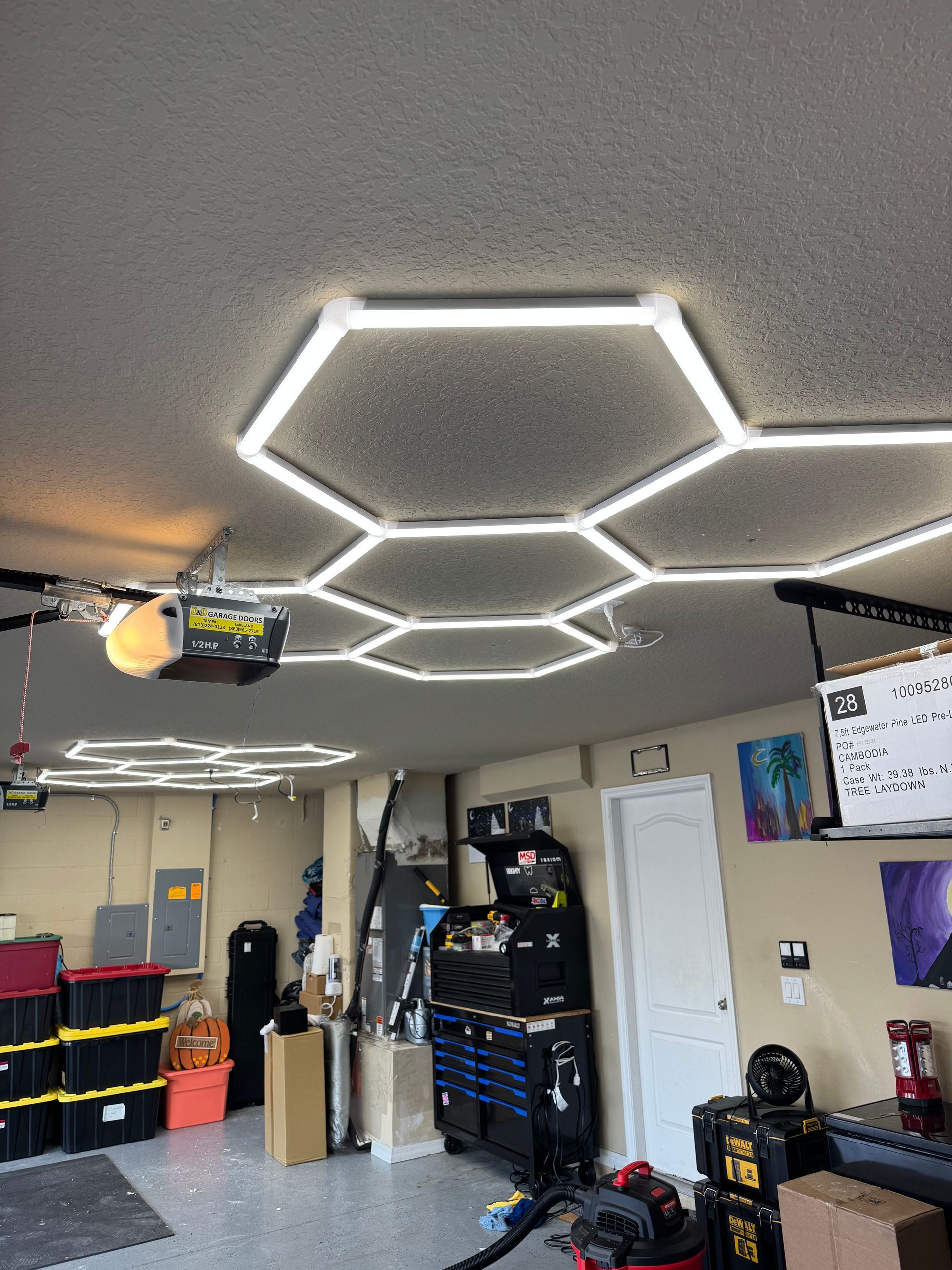 Hexagonal LED ceiling lights in a garage with tools, cabinets, and a wall-mounted TV.