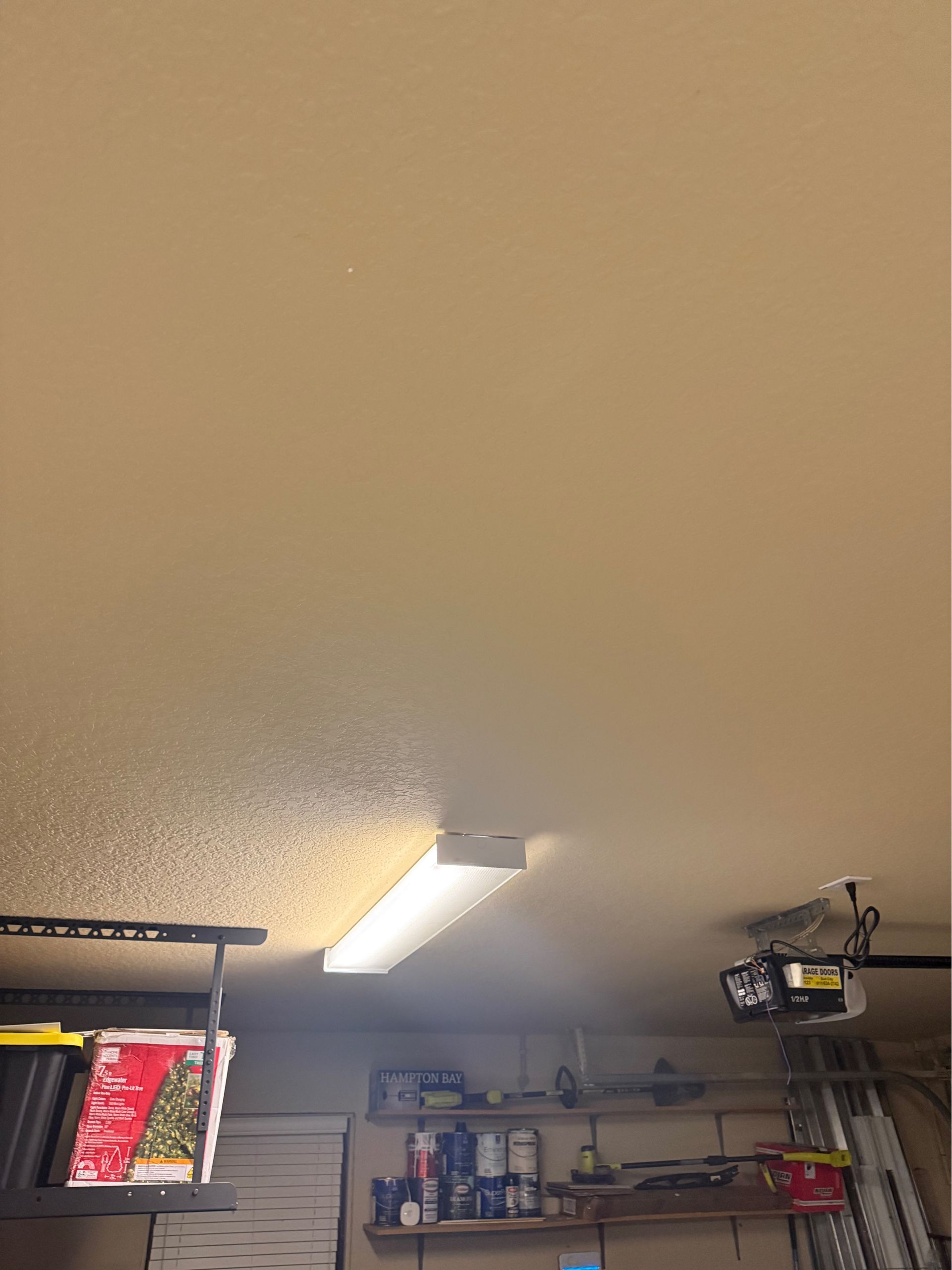 Garage ceiling with bright fluorescent light, shelves of tools and supplies, and a bike rack in the corner.