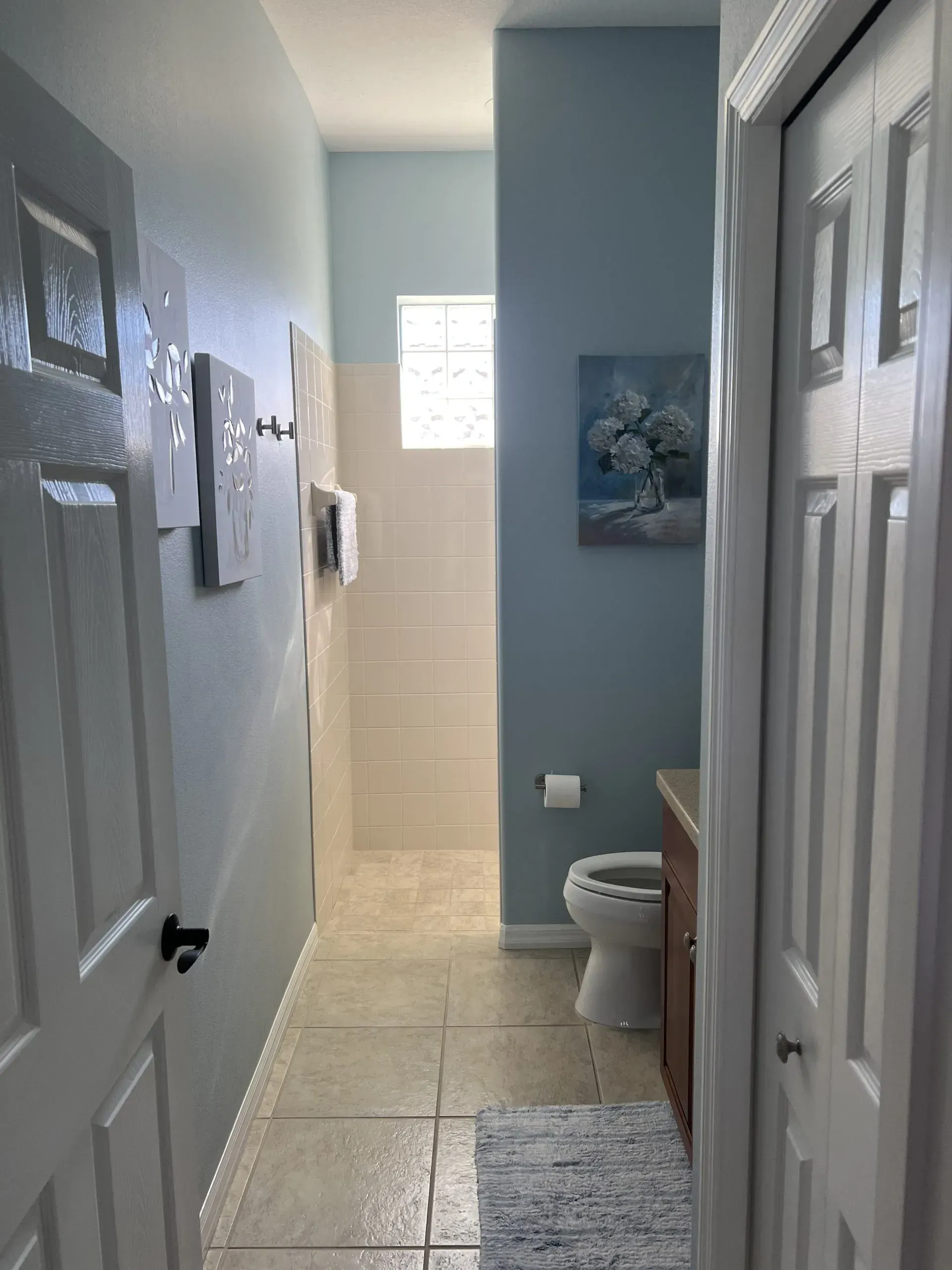 Narrow bathroom hallway with white walls, tiled floor, and a toilet visible at the far end.