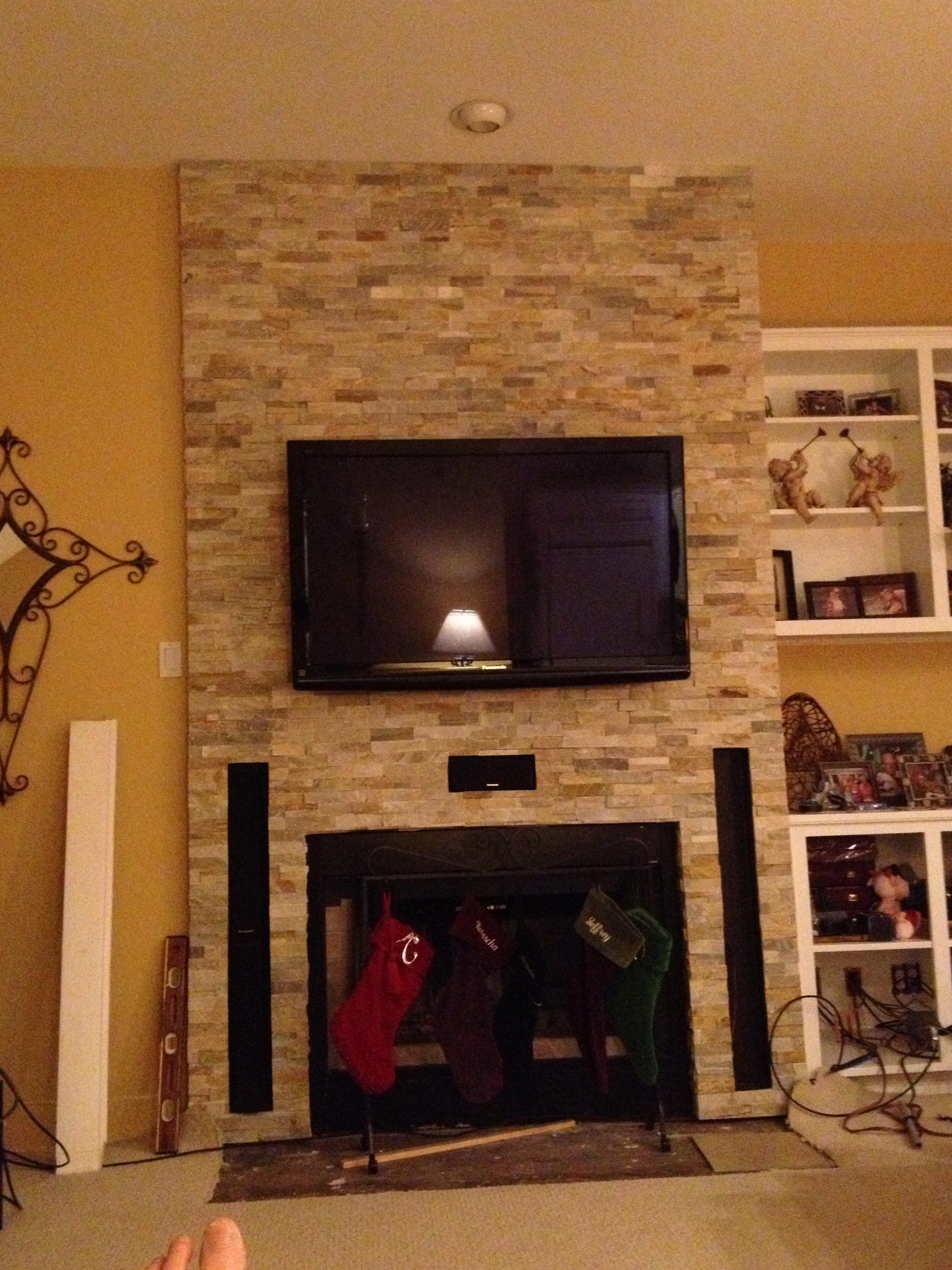 Living room with stone fireplace, wall-mounted TV, and built-in shelves decorated for Christmas.