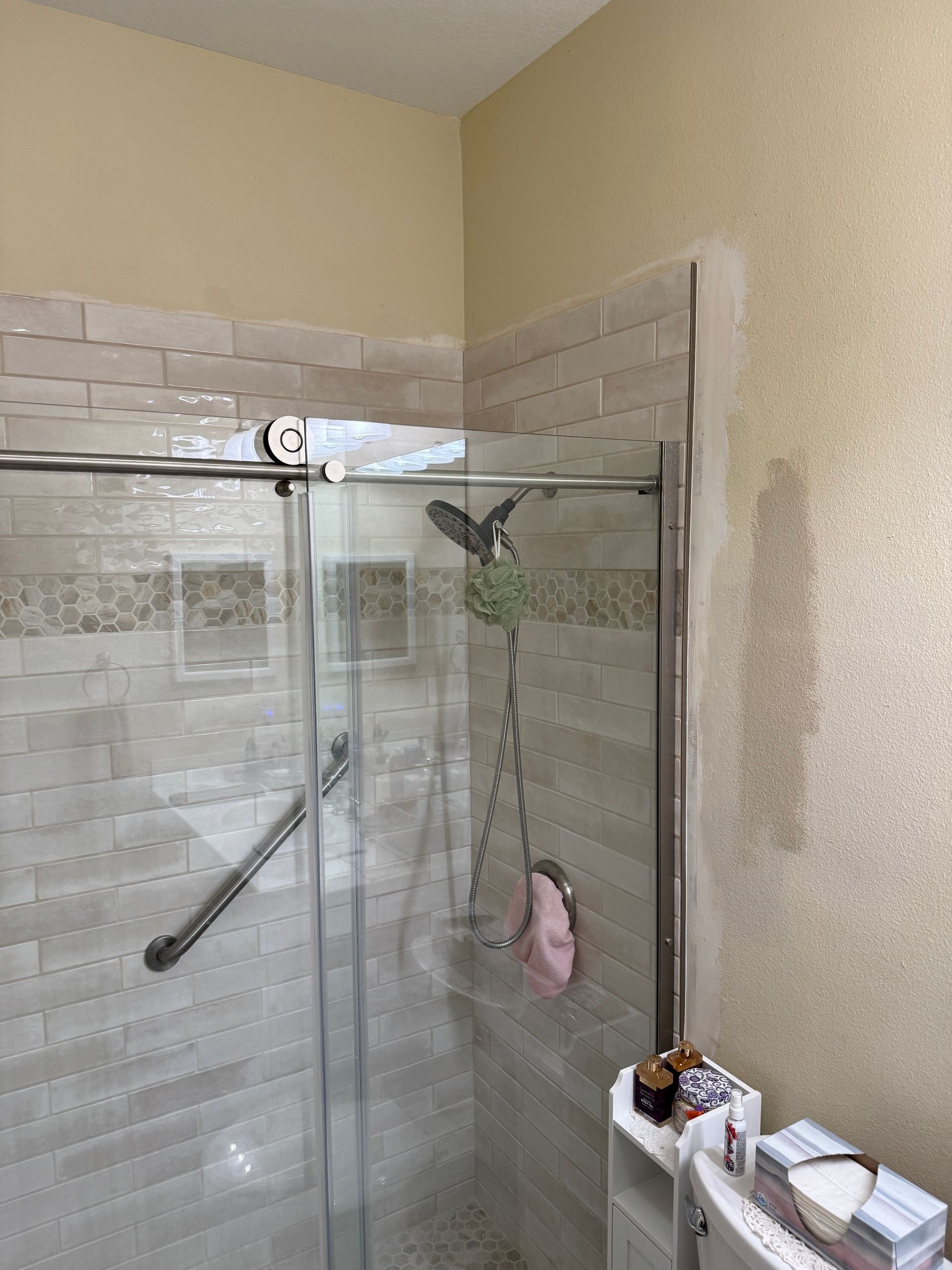 Glass shower stall with tiled walls, silver grab bar, and pink shower loofah in a bathroom
