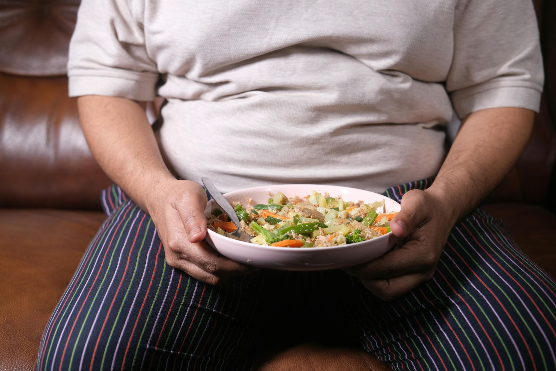 Un hombre está sentado en un sofá sosteniendo un tazón de comida.