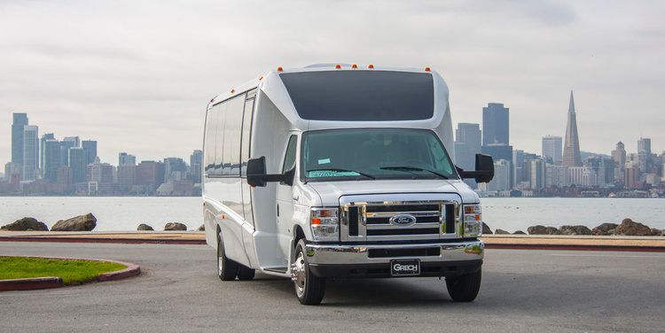 A white van is parked on the side of the road in front of a city skyline.
