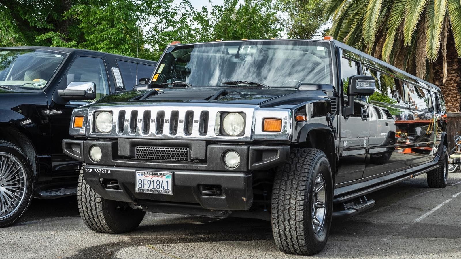 A black hummer limousine is parked next to a black truck in a parking lot.