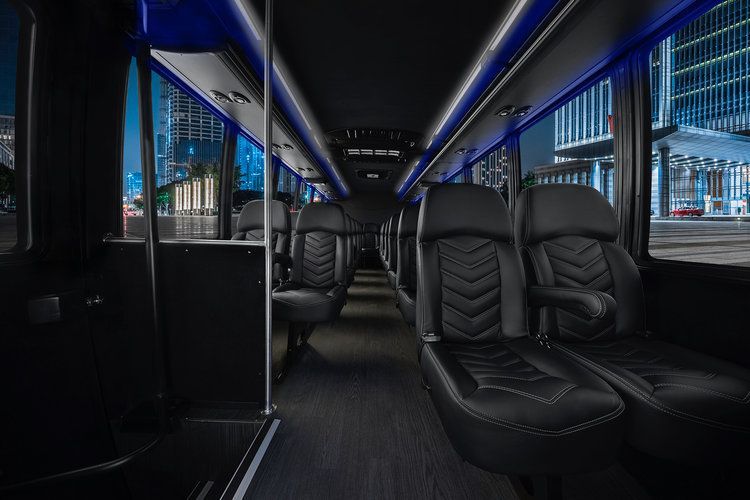 Interior of a black bus with black leather seats, blue lighting, and a city view through the windows.