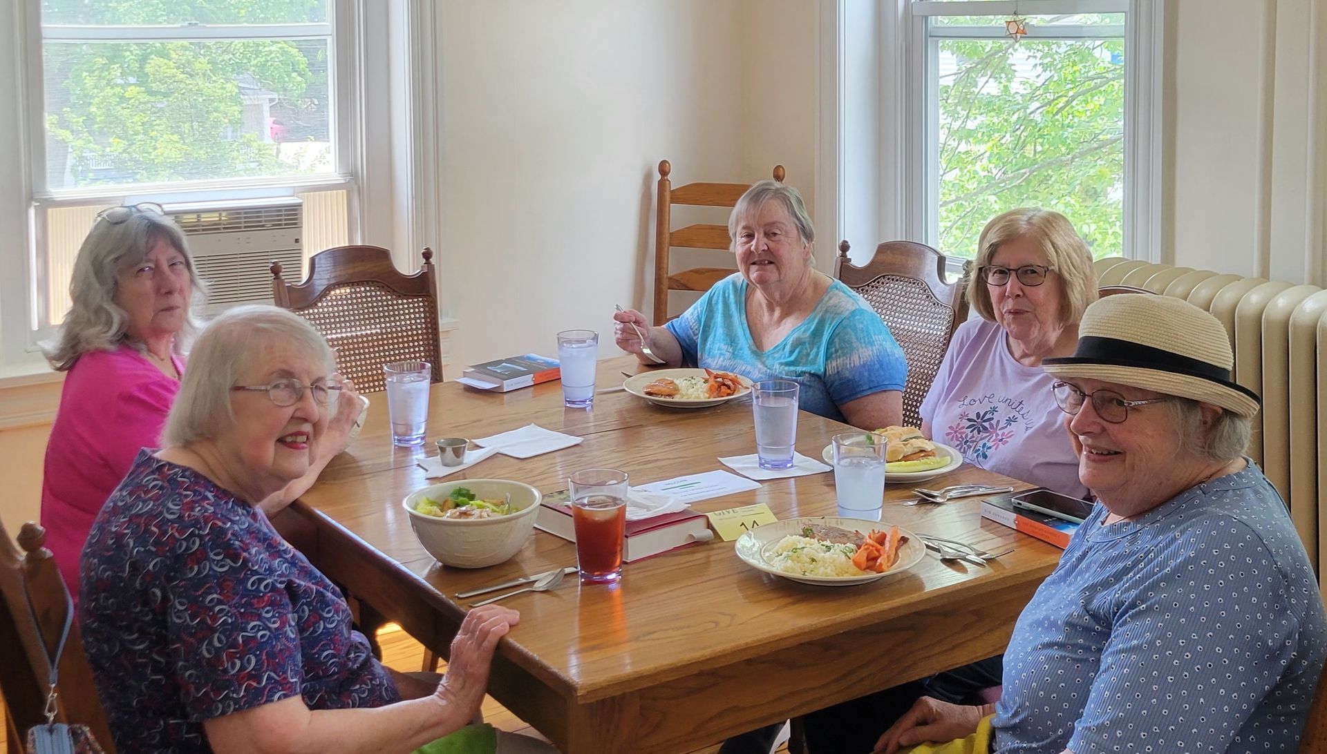 Six people seated at a table, eating. Sunlight streams through windows.