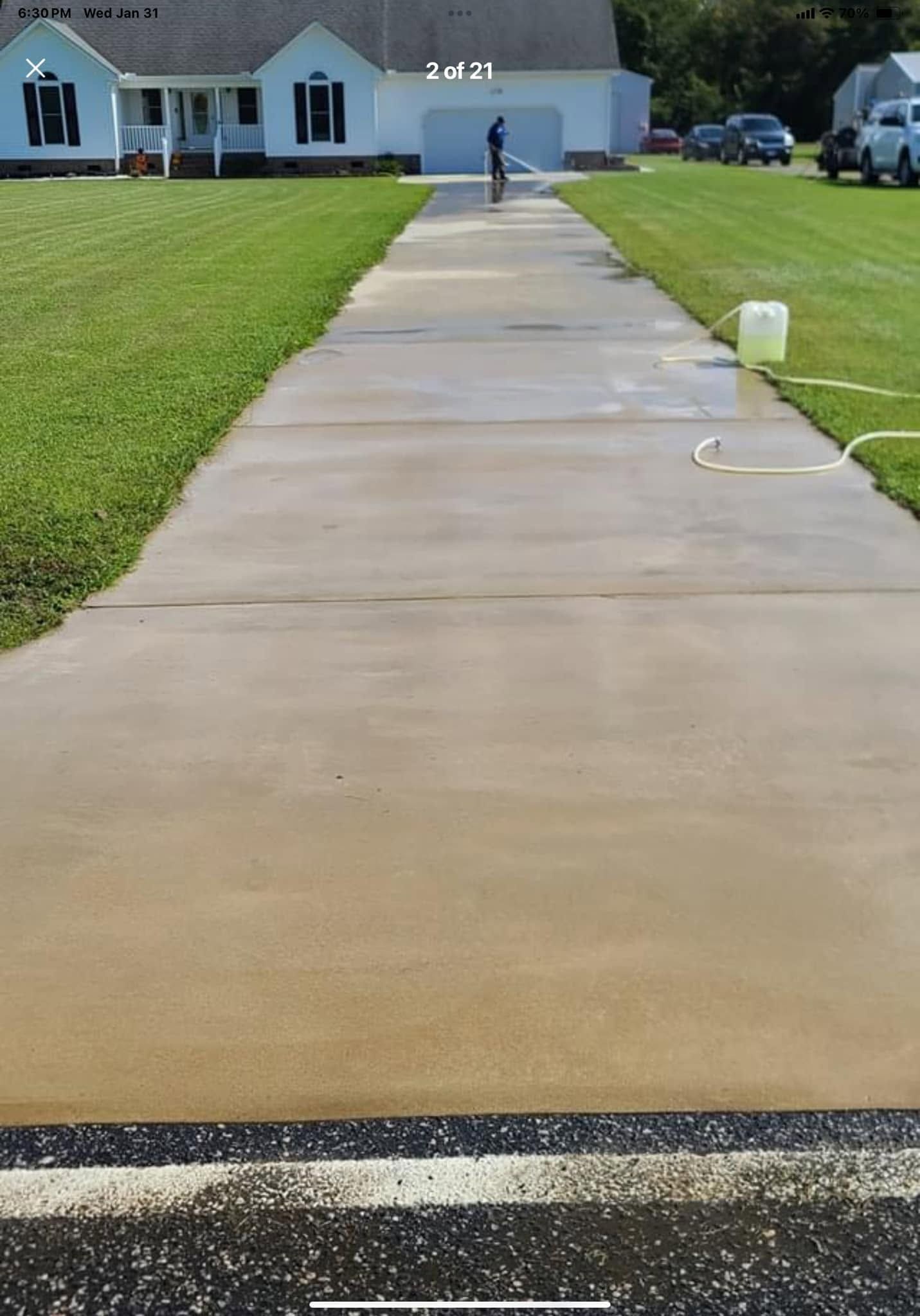 Freshly sealed concrete driveway leading to a suburban house with green lawns and a worker in the distance
