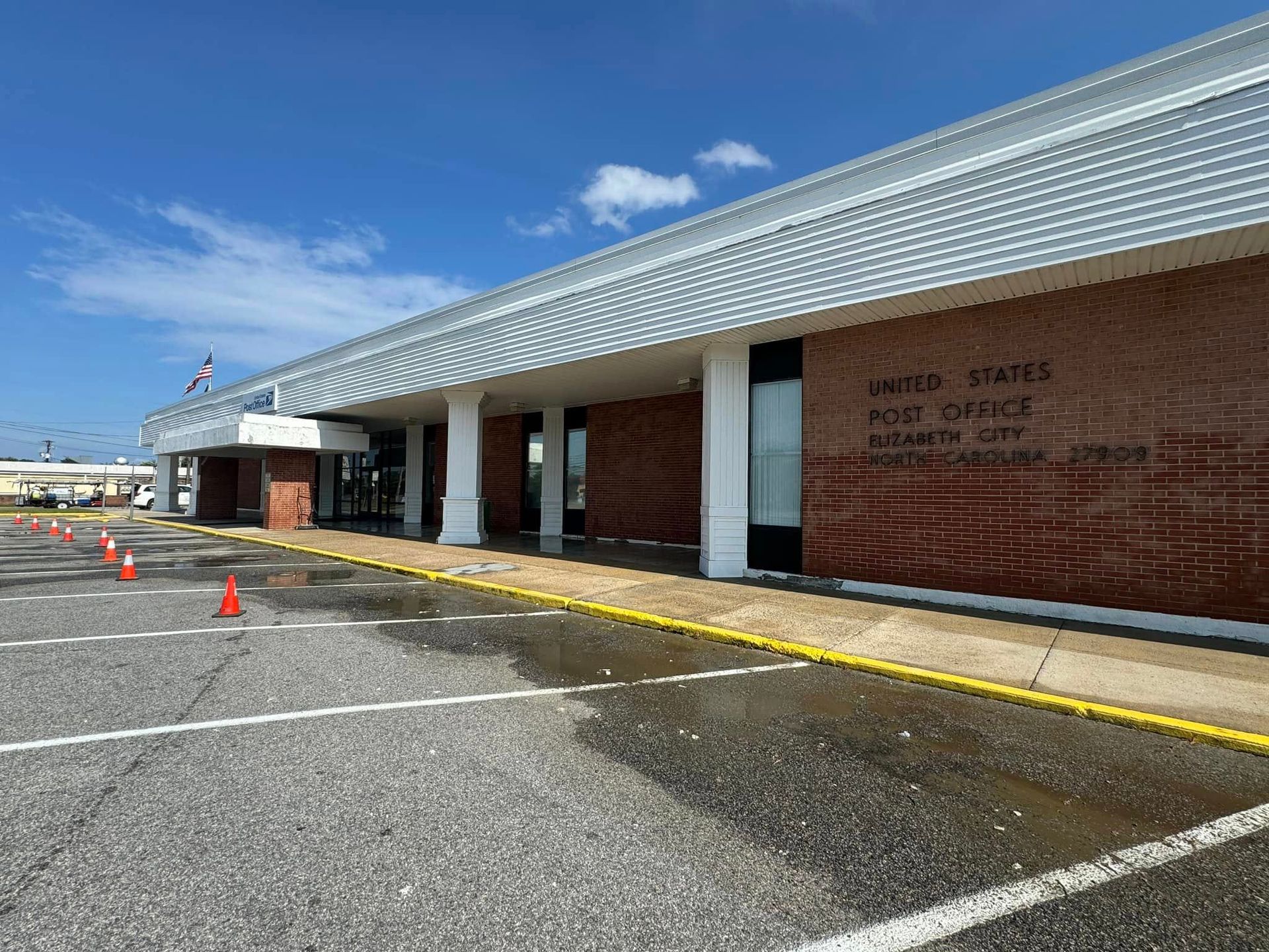 Airport terminal entrance with red brick walls, white columns, and orange cones in a parking lot under a blue sky