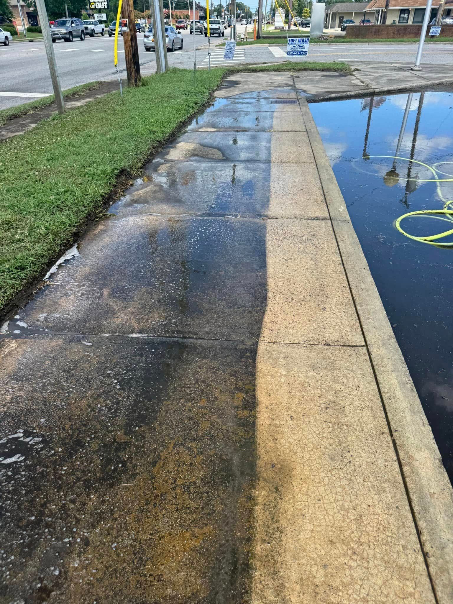 Wet sidewalk beside a flooded road, with a curb and yellow lane markings reflected in water.