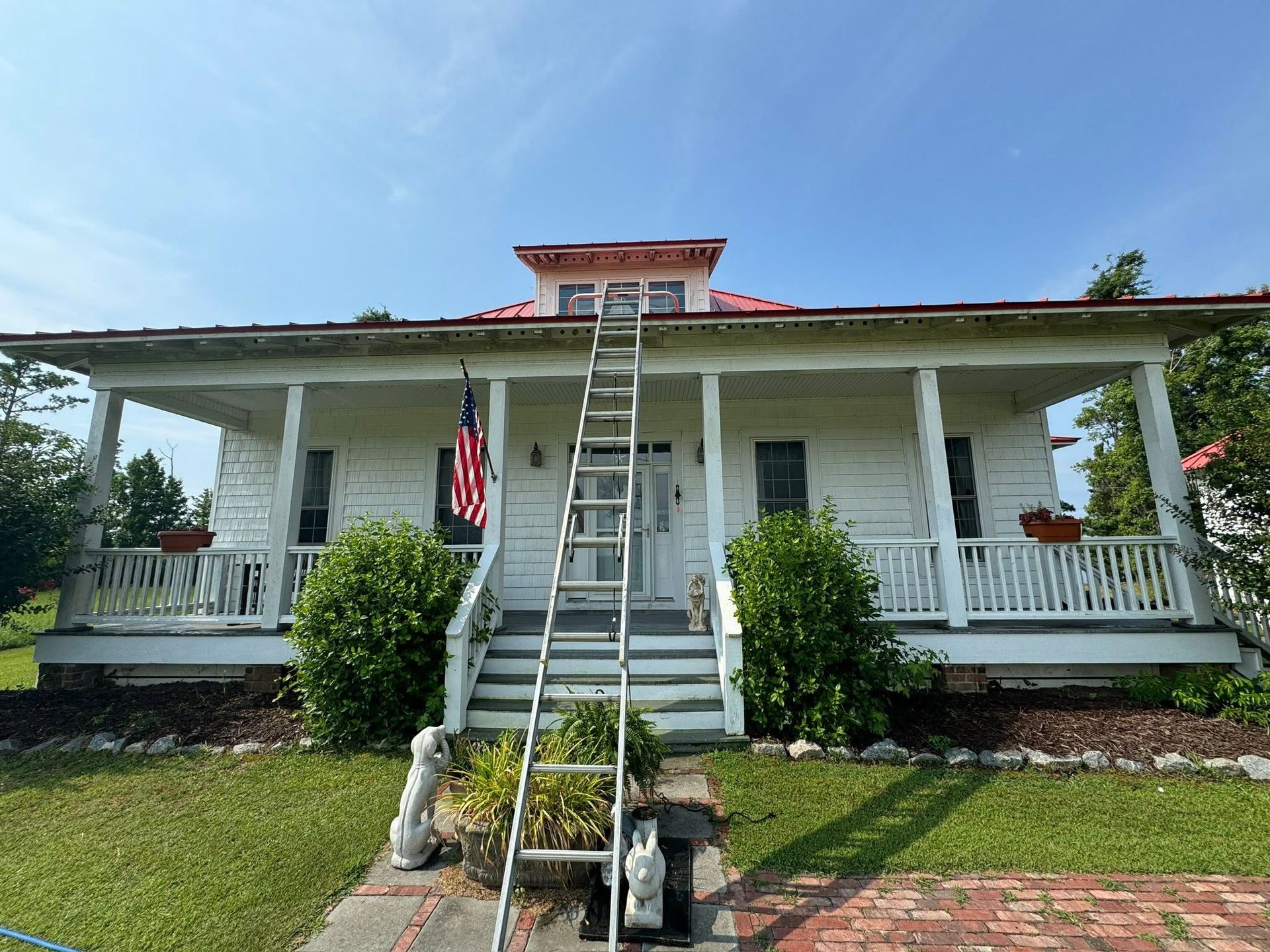 White house with front porch and stairs, centered ladder reaching the roof under a blue sky.