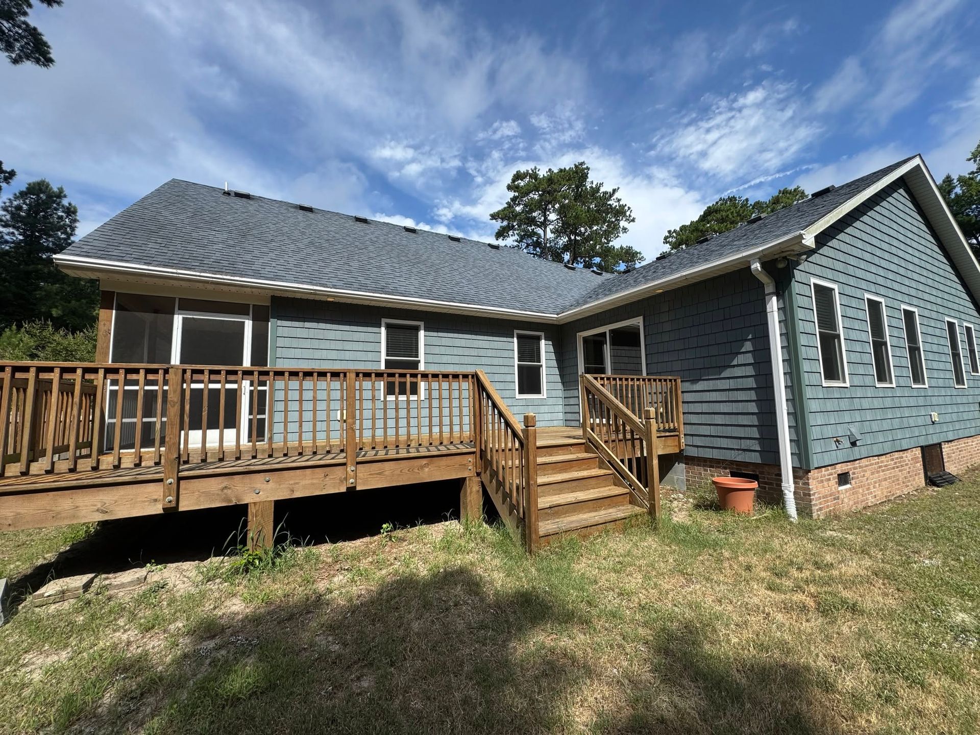 Single-story gray house with a wooden ramp and porch under a cloudy sky.