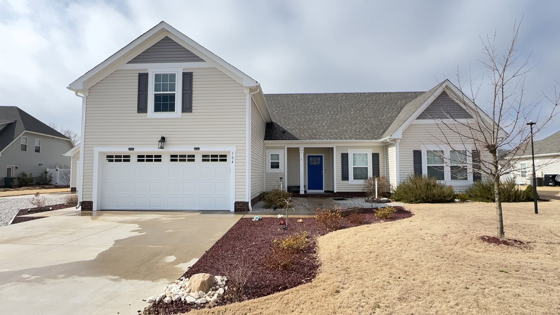 Suburban beige house with two-car garage, blue front door, and a snow-dusted lawn