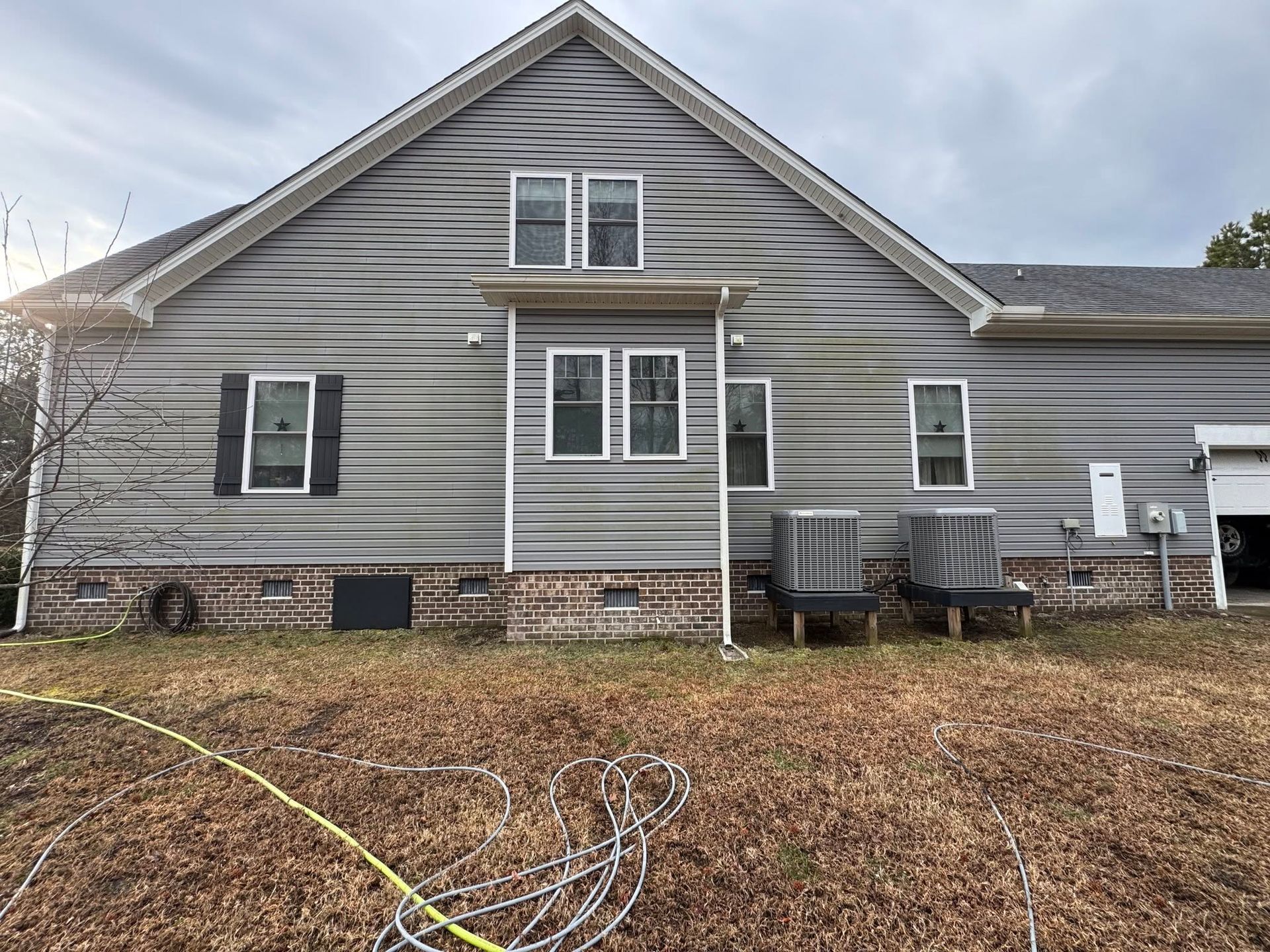 Gray house exterior with white trim, dormer window, and patio furniture in a leaf-covered yard
