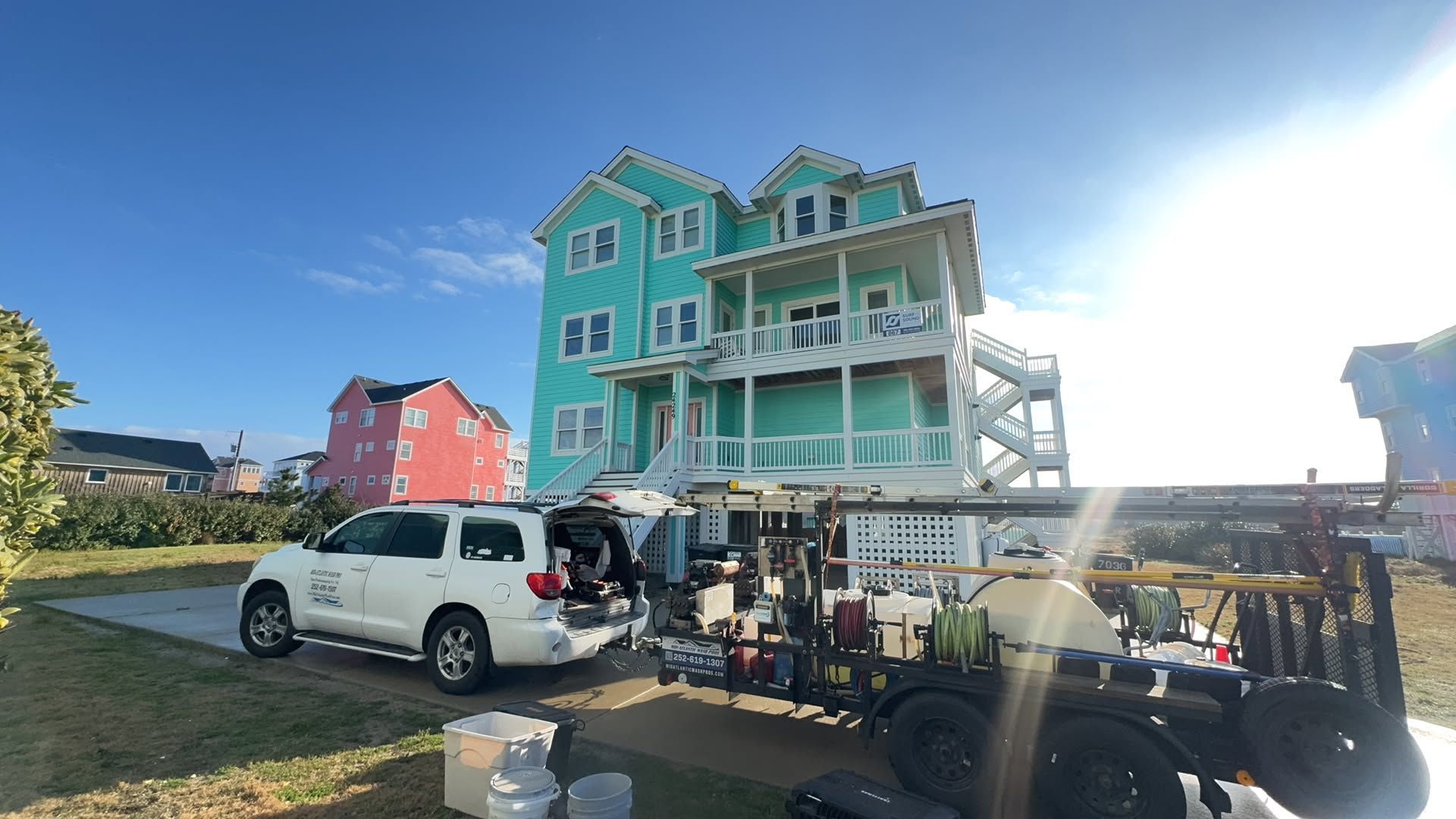 White SUV parked by a turquoise beach house with balconies under bright sun